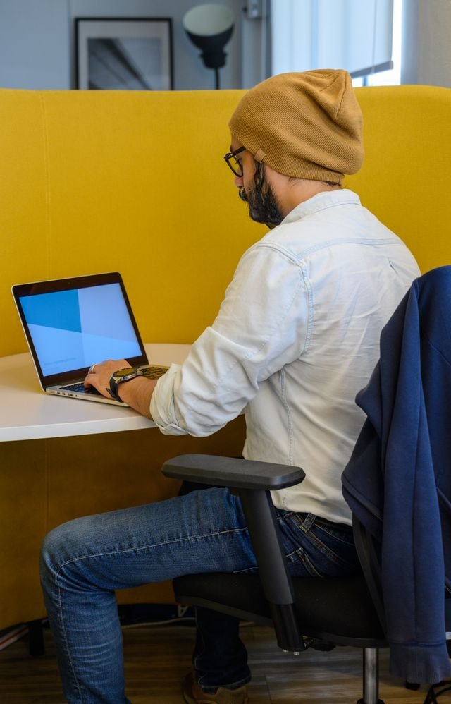 Bearded man in casual attire working on a laptop in modern office setting.